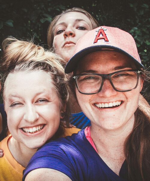 Drei lachende Personen machen im Freien ein Selfie und schauen fröhlich in die Kamera.